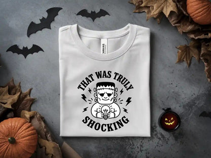 White t-shirt with Frankenstein's monster holding a glowing lightbulb and text "That Was Truly Shocking".